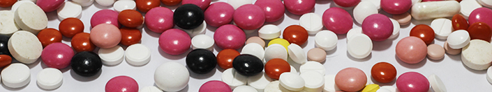 Image of different pills scattered on a surface in reds, pinks, whites, and yellows